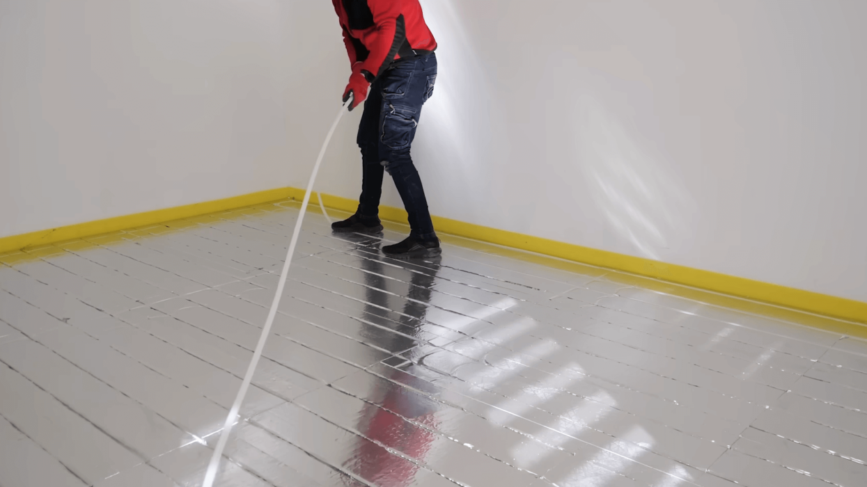 Instalator ogrzewania w czerwonej bluzie i rękawiczkach układa rury grzewcze w pomieszczeniu, przygotowując powierzchnię do dalszych prac.