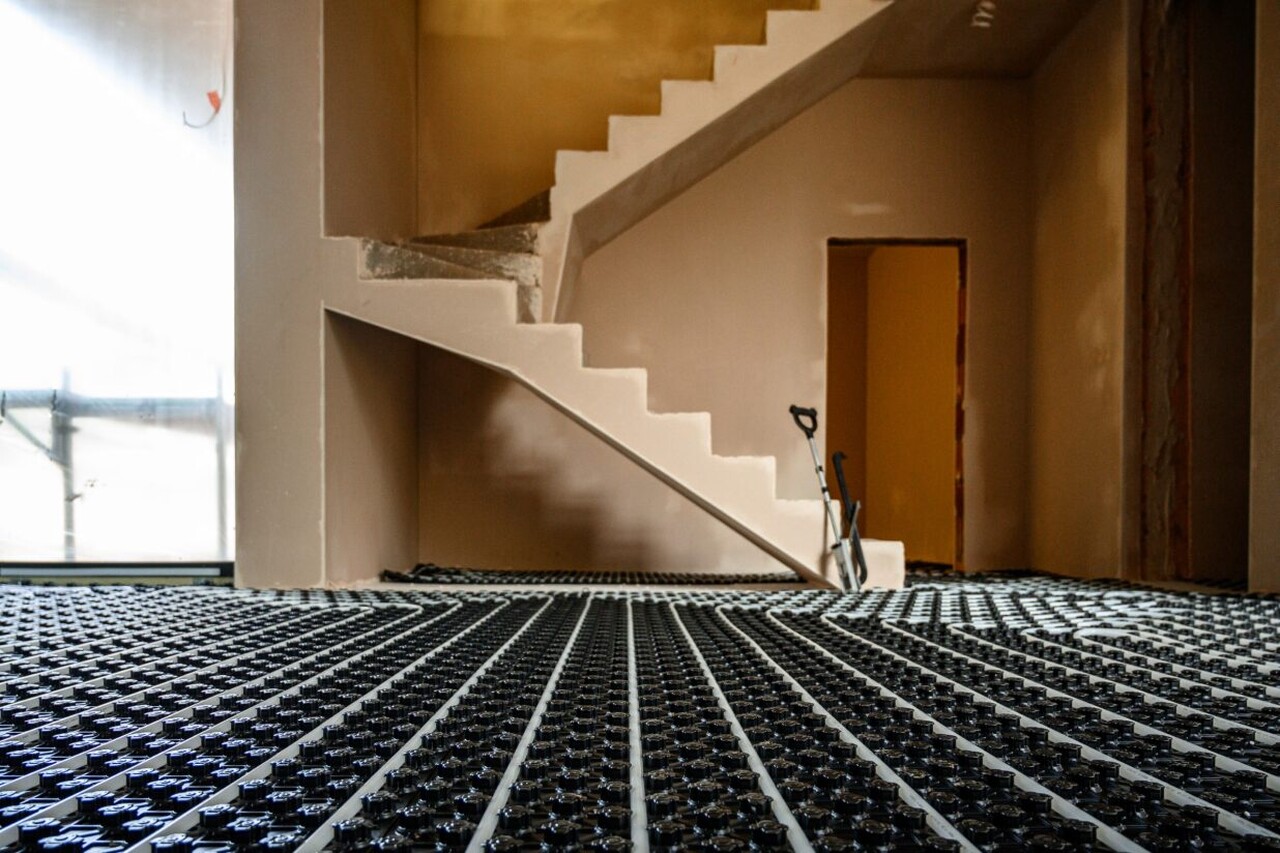 Instalacja ogrzewania podłogowego w nowoczesnym wnętrzu z widocznymi schodami betonowymi.